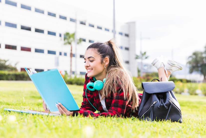 smiling-young-woman-laying-lawn-reading-book-university-campus_23-2148093571